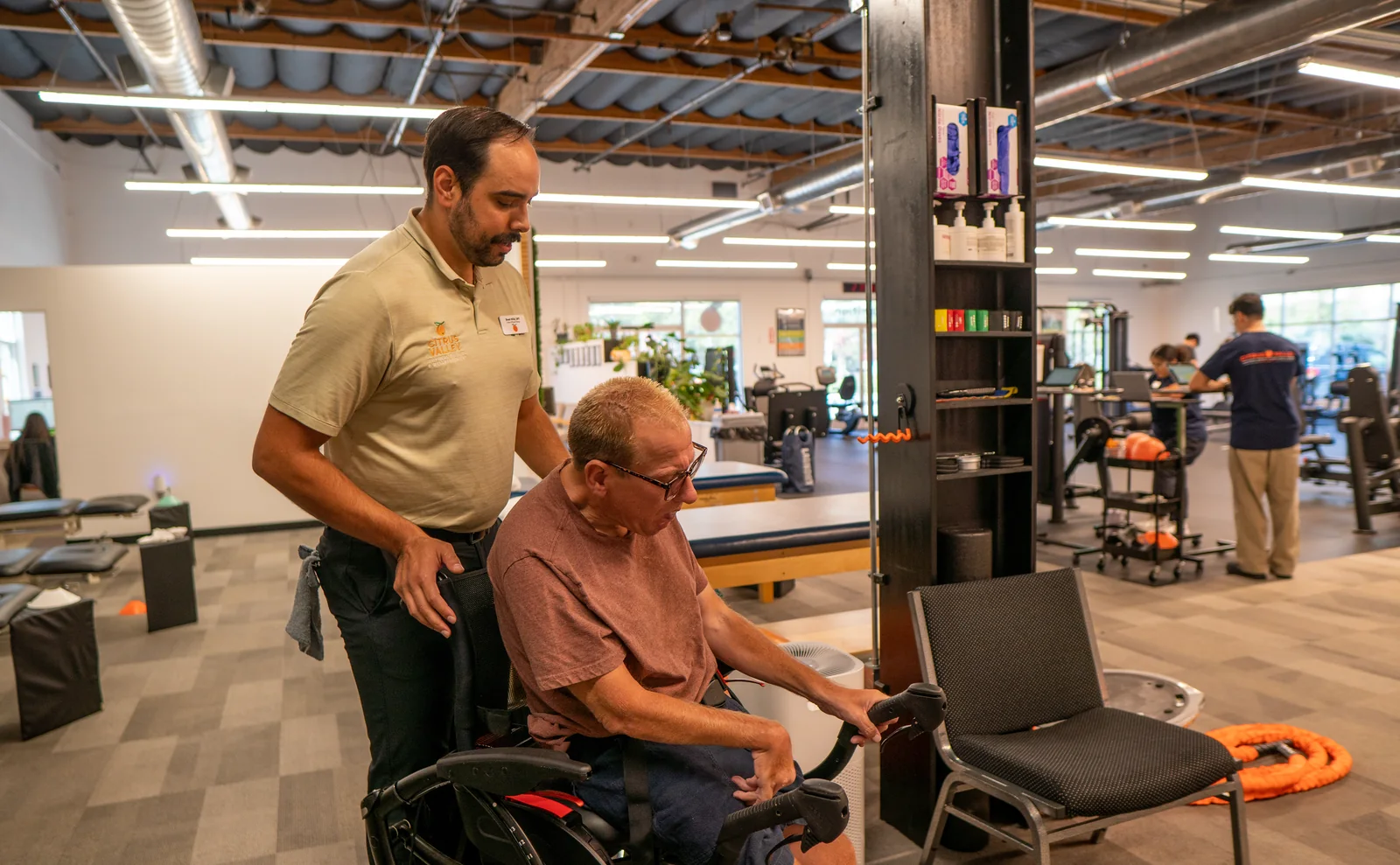 Physical therapist assisting a patient in a wheelchair on the Citrus Valley gym floor