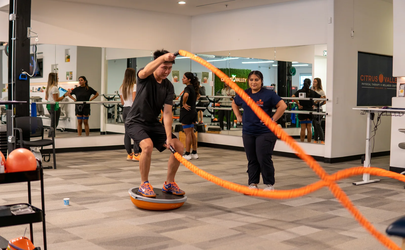 Patient swinging battle ropes on a balance trainer while a therapist coaches